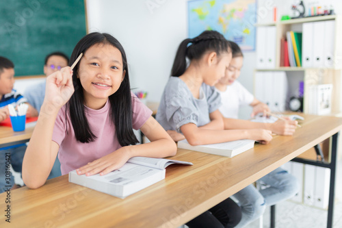asian girl use pencil and touch her head,  asian student group do homework in classroom, they sharing knowledge together, they explaining about important lesson to friends, happiness elementary school
