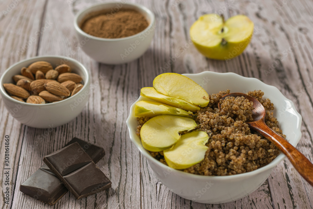 Apple slices in a bowl of quinoa and chocolate porridge on a wooden table.