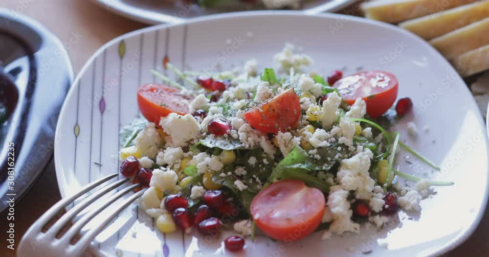Fresh made arugula salad with cherry tomatoes, soft cheese, sweetcorn kernel and pomegranate seed on plate on rotating stand, close up Fresh made arugula salad with cherry tomatoes, soft cheese, sweetcorn kernel and pomegranate seed on plate on rotating stand, close up
