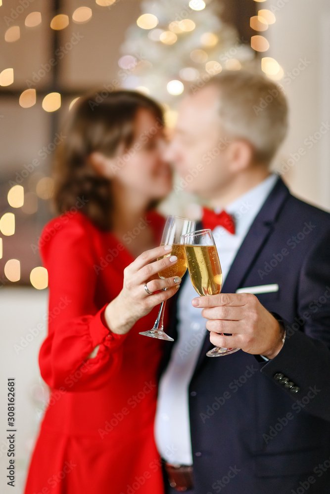Happy couple of people with two glasses of champagne on the background of Christmas lights in a bright studio. Object out of focus. Close-up. Happy couple of people with two glasses of champagne on the background of Christmas lights in a bright studio. Object out of focus. Close-up.