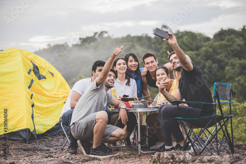 Camping season, Group of campers are having fun talking and taking selfies together with full kitchen equipment on the table.
