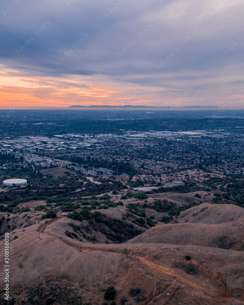Aerial view of open rolling hills in suburban Southern California.  Radio tower atop hill during sunset surrounded by mountains and ocean