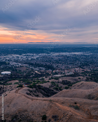Aerial view of open rolling hills in suburban Southern California. Radio tower atop hill during sunset surrounded by mountains and ocean