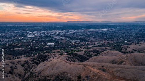 Aerial view of open rolling hills in suburban Southern California.  Radio tower atop hill during sunset surrounded by mountains and ocean