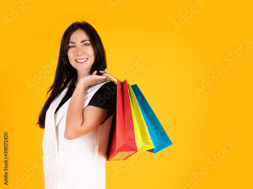 Beautiful shopper woman smiling and holding colorful shopping bag after enjoy buy fashion clothes with discount sale on yellow isolated background with copy space