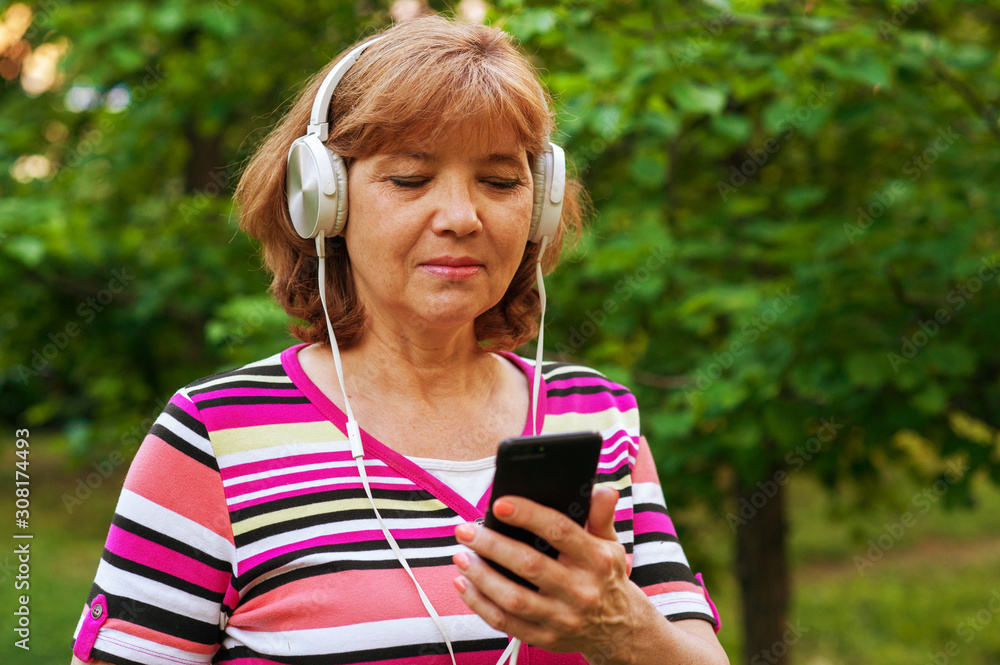 60 year old beautiful woman in headphones and phone in her hands in  summer in park
