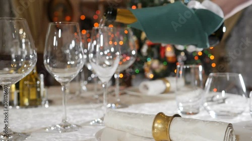 Pouring champagne in slow motion with blurred Christmas lights, flashing garland in background. Xmas and New Year celebration. Table setting, decoration concept. Shot in hd photo