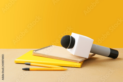 Microphone and notebooks on table against color background