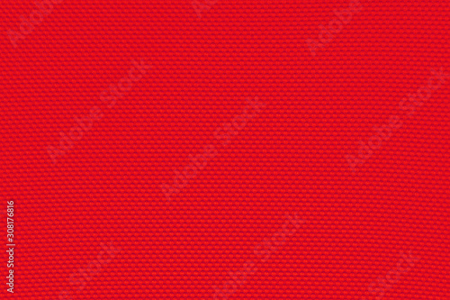 Deep saturated red background from a textile material with pattern, closeup. Structure of venetian red colored fabric with punching texture. Perforated cloth backdrop.
