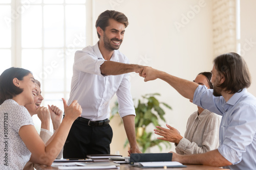 Happy young male team leader bumping fists with smiling teammate.