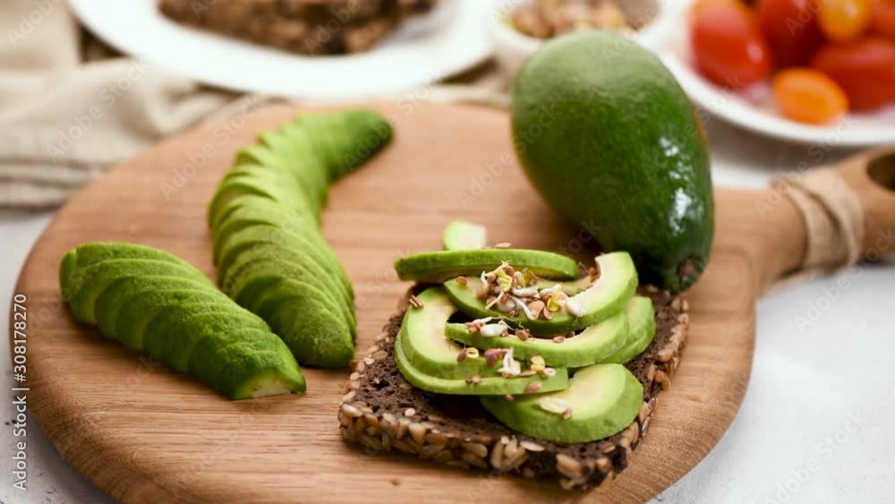 Seasoning avocado sandwich. Woman's hand add sprouts and seeds on top of healthy avocado and rye bread toast. Vegan, vegetarian food concept Seasoning avocado sandwich. Woman's hand add sprouts and seeds on top of healthy avocado and rye bread toast. Vegan, vegetarian food concept