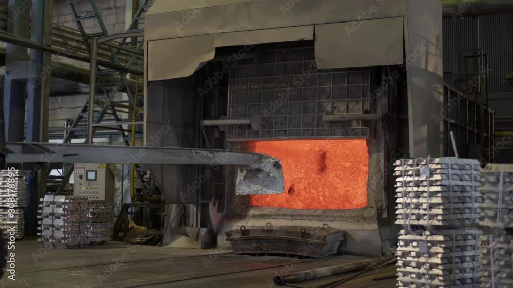 Loader mixes molten aluminum in a blast furnace. Aluminium foundry furnace loaded with metal. Red hot flames glowing and liquid melting. Fire melts aluminum ingots in a blast furnace. Loader mixes molten aluminum in a blast furnace. Aluminium foundry furnace loaded with metal. Red hot flames glowing and liquid melting. Fire melts aluminum ingots in a blast furnace.