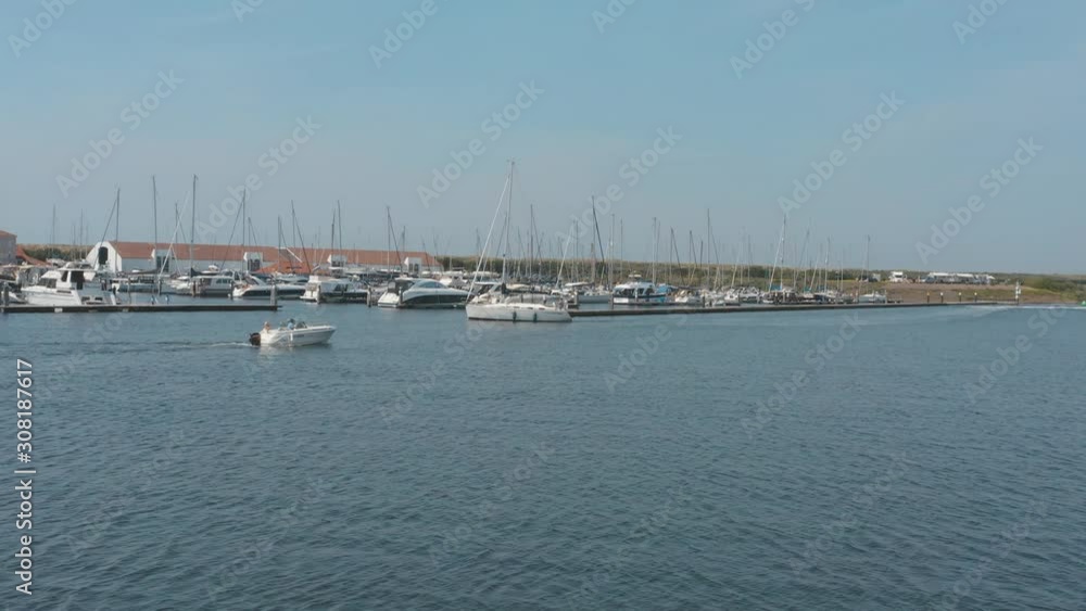 Cinematic drone / aerial shot of a motor boat with a marina in the background with sailing boats on a sunny day, 30p Cinematic drone / aerial shot of a motor boat with a marina in the background with sailing boats on a sunny day, 30p