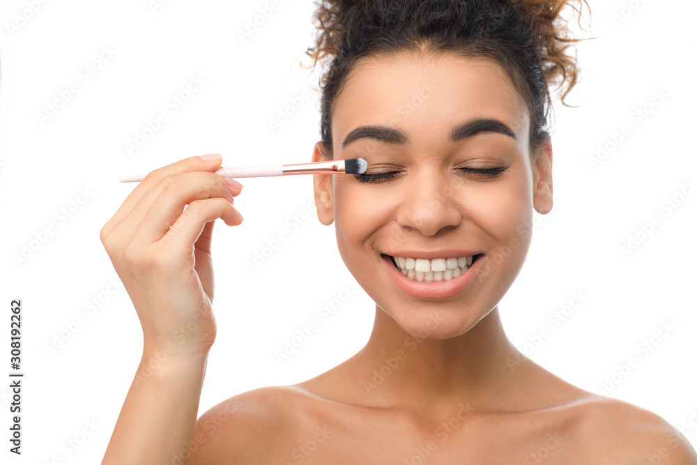 Happy black woman applying eyeshadows with brush