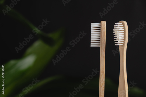 Close up of two bamboo toothbrushes and green leaf on a dark background. Bathroom essentials. Dental care and zero waste concept.