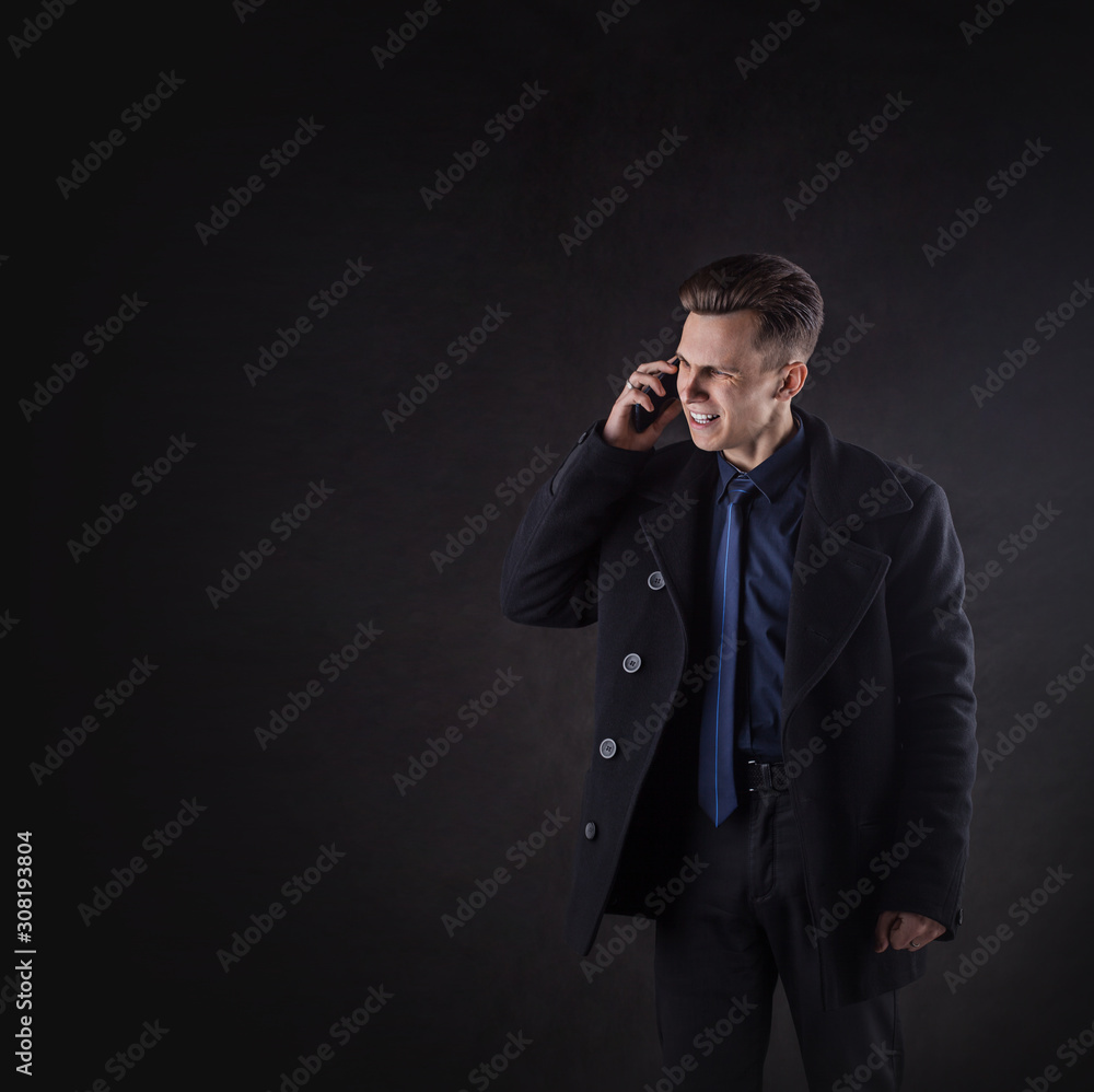 A handsome man in a coat screams while talking on the phone. Business concept on a dark background. Stress A handsome man in a coat screams while talking on the phone. Business concept on a dark background. Stress