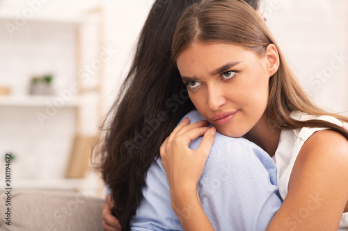 Fototapete Girl Rolling Eyes Embracing Crying Friend Sitting On Sofa