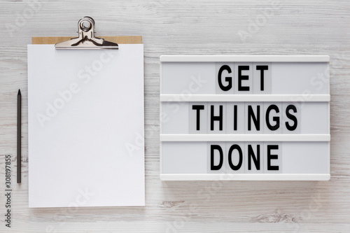 Fotografie 'Get things done' words on a modern board, clipboard with blank sheet of paper on a white wooden background, top view