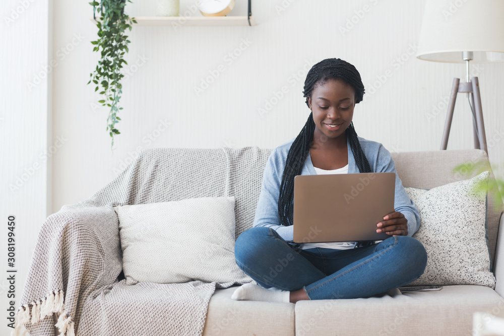 Black millennial woman working with laptop computer on sofa at home Black millennial woman working with laptop computer on sofa at home
