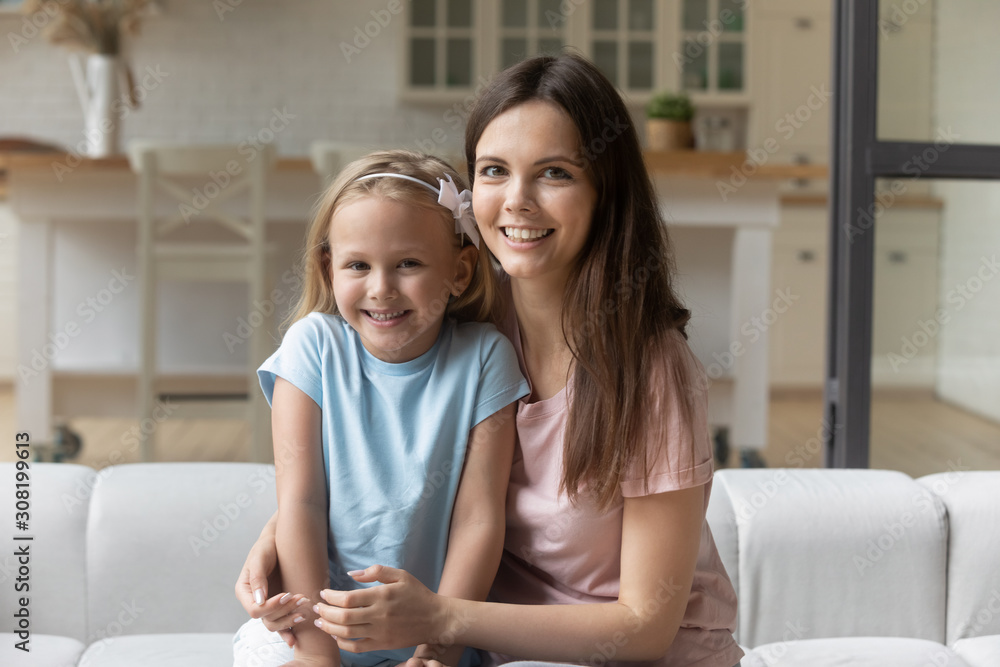Babysitter and girl hugging seated on couch looking at camera Babysitter and girl hugging seated on couch looking at camera