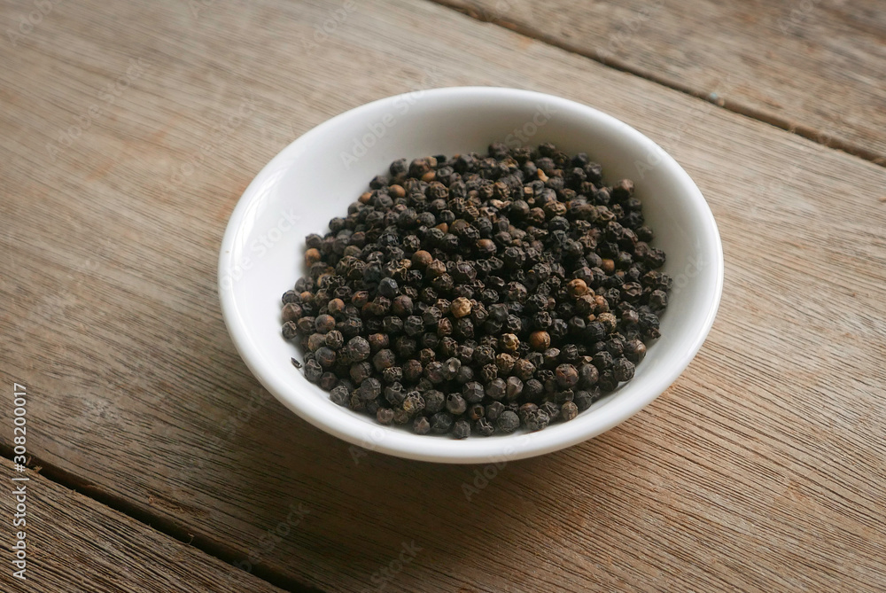 Black pepper in a white plate on wooden background. Black pepper in a white plate on wooden background.