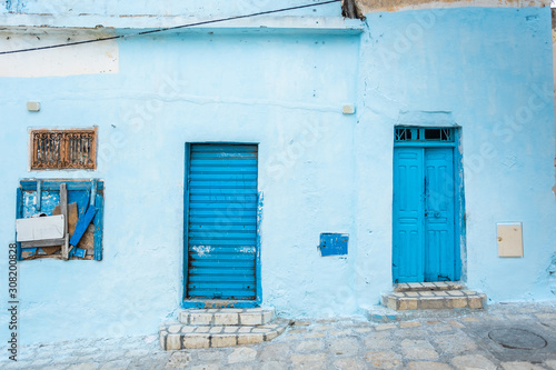 Blue wall of old building and two painted doors and one window. Tunisia. Horizontal color photography.