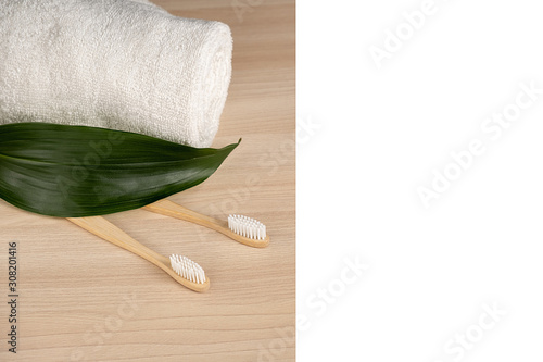 Fototapeta Naklejka Na Ścianę i Meble -  Eco natural bamboo toothbrush, white frame and towel on wooden background with green leaf. Zero waste concept. Plastic free essentials, teeth care. Sustainable lifestyle
