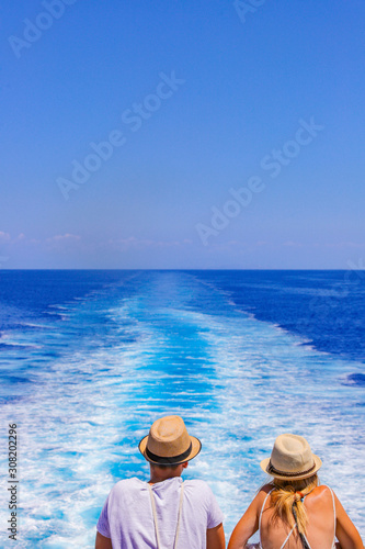 Tourists with a straw hat stand on the deck of a cruise ship and look out over the ocean  While the boat is sailing. Couple are looking at the sea as they stand at the edge of the ship's deck. © MagioreStockStudio