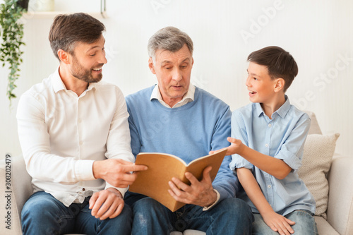 Grandfather Reading Book With Mature Son And Grandson At Home