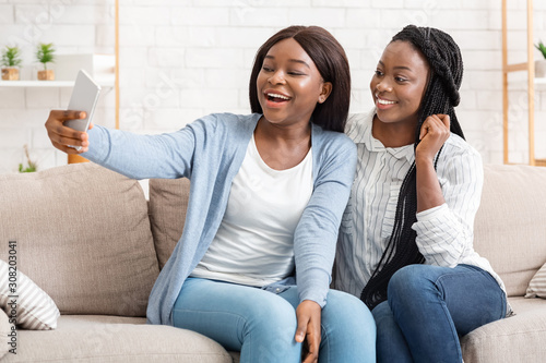 Two black female friends taking selfie, having fun at home