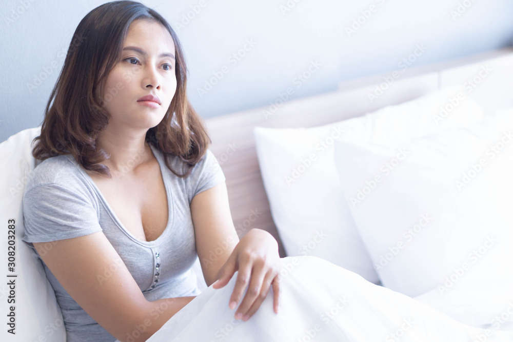 Closeup woman sitting on bed in the bedroom with thinking or depressed feeling, selective focus