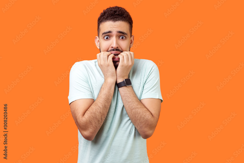 Portrait of stressed out nervous brunette man with beard biting nails, looking frightened and shocked about problems, suffering anxiety and panic. indoor studio shot isolated on orange background Portrait of stressed out nervous brunette man with beard biting nails, looking frightened and shocked about problems, suffering anxiety and panic. indoor studio shot isolated on orange background