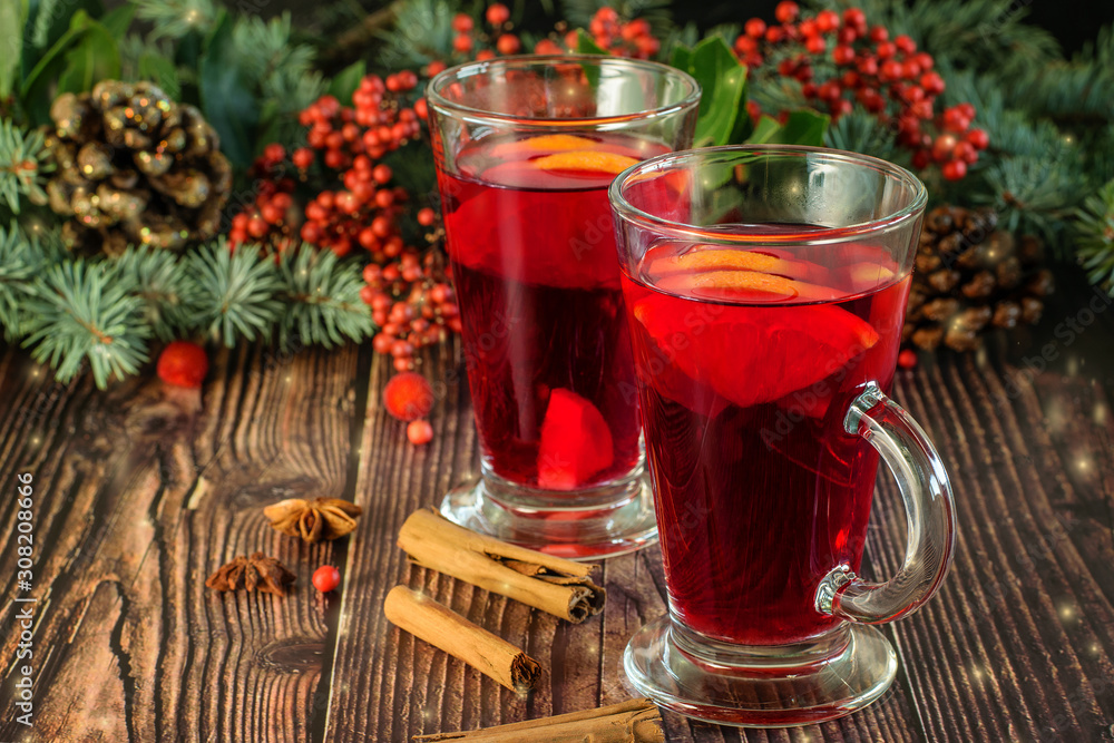 Hot traditional drink Mulled wine on the wooden brown background closeup. Christmas and New Year vignette of branches of blue fir, pinecones and red berries. Holidays decoration with lights. Hot traditional drink Mulled wine on the wooden brown background closeup. Christmas and New Year vignette of branches of blue fir, pinecones and red berries. Holidays decoration with lights.