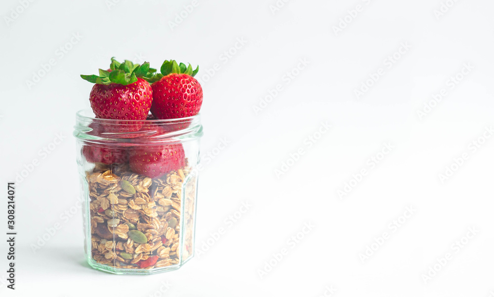 Fresh strawberries with green leave head on top of healthy muesli granola in clear glass bottle on white background with copy space, for banner Fresh strawberries with green leave head on top of healthy muesli granola in clear glass bottle on white background with copy space, for banner