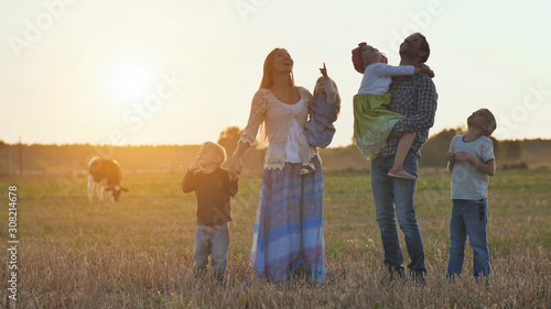 A large family goes on the field in the village during sunset.