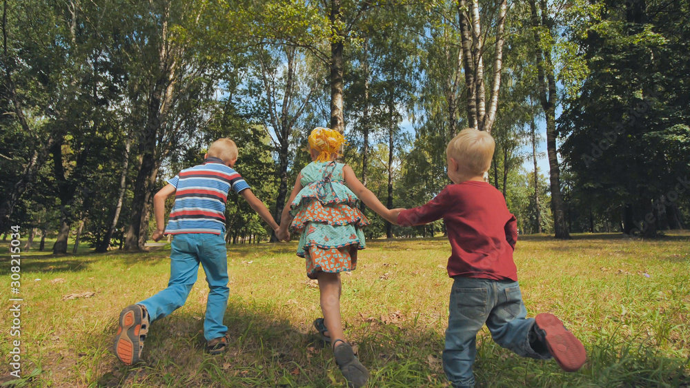 Three cheerful children are holding hands running in the park.