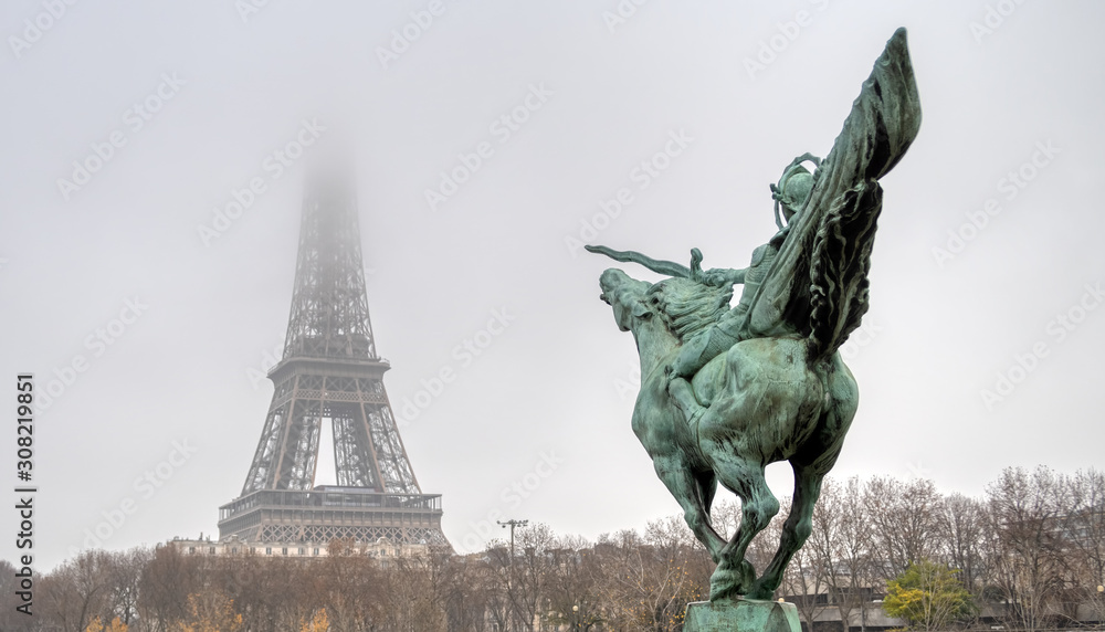 Top of the Eiffel Tower lost in the mist with Bir-hakeim statue La France Renaissante in foreground - Paris, France