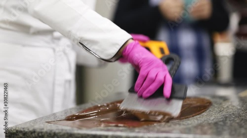 pastry chef in white uniform and pink gloves tempers chocolate on a marble plate using a scraper and pyrometer