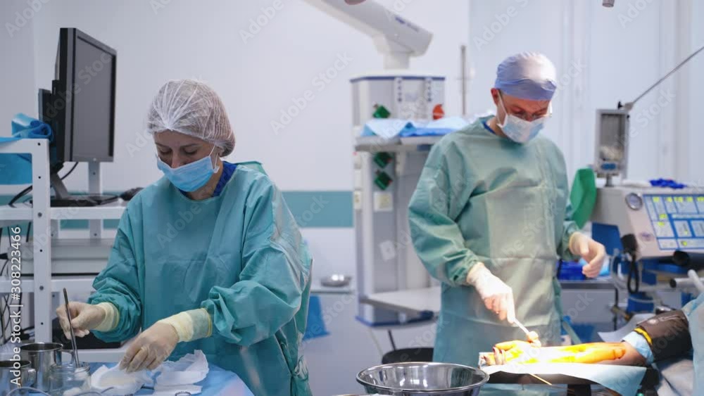 Nurse assists surgeon during the operation. Professional doctor in medical uniforms performs an operation on patient's arm. Female assistant helps specialist in clinic. Nurse assists surgeon during the operation. Professional doctor in medical uniforms performs an operation on patient's arm. Female assistant helps specialist in clinic.