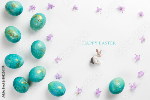 Happy easter card. Stylish minimalistic composition of turquoise with gold easter eggs on a white background. Figurine of a rabbit and delicate spring flowers. Flat lay, top view, copy space