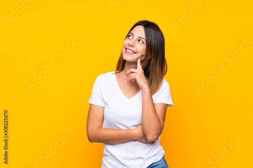 Young woman over isolated yellow background thinking an idea while looking up photo