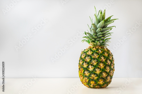 a whole ripe pineapple stands on a white surface with a light gray background.