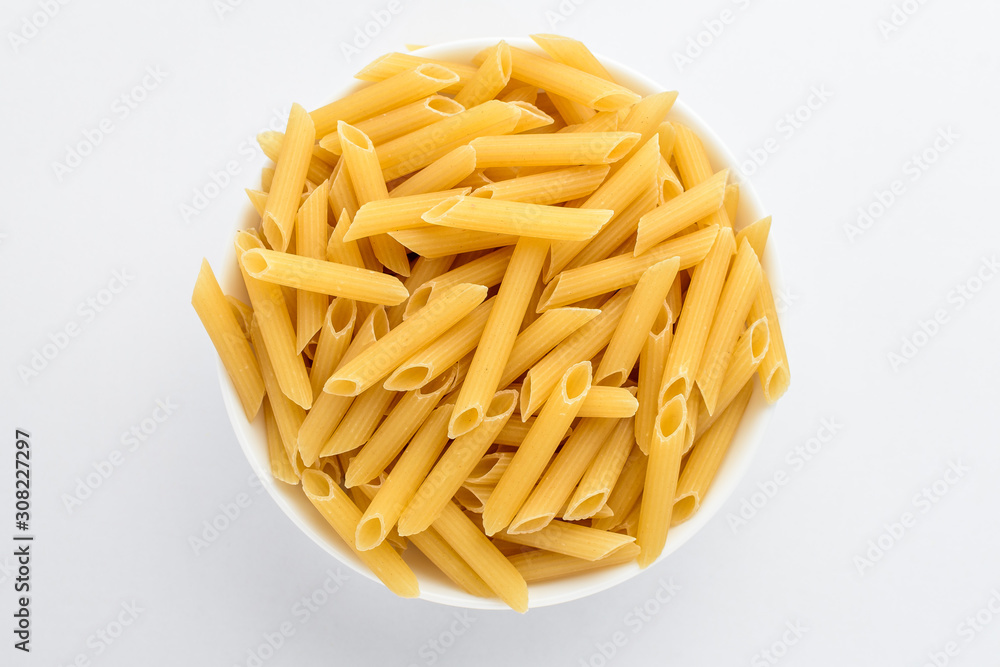 Dried penne Italian pasta in a round bowl ready to be cooked, isolated on white table, top view or flat lay of healthy food Dried penne Italian pasta in a round bowl ready to be cooked, isolated on white table, top view or flat lay of healthy food