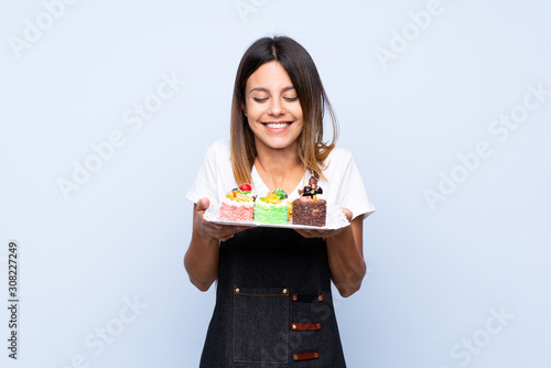 Young woman over isolated blue background holding mini cakes