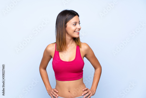 Young sport woman over isolated blue background posing with arms at hip and looking side