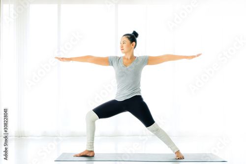 close up Asian yogi woman practicing yoga, standing in Warrior two exercise, Virabhadrasana II pose on mat, working out , full length , white yoga studio, Concept of healing body and spirit.