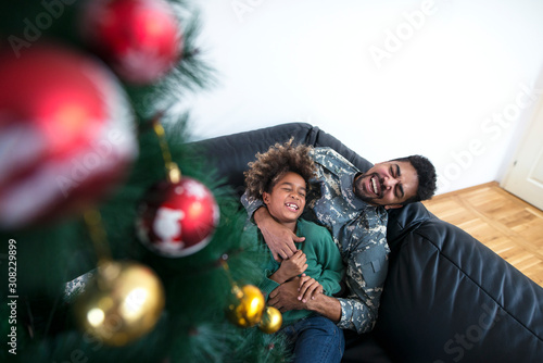 Soldier spending Christmas with his family at home. Man in uniform having fun with his daughter by Christmas tree. Happy moments.