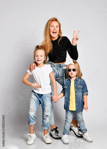 Young happy mother is posing with her daughters, showing two victory sign gesture. Human relations, family.