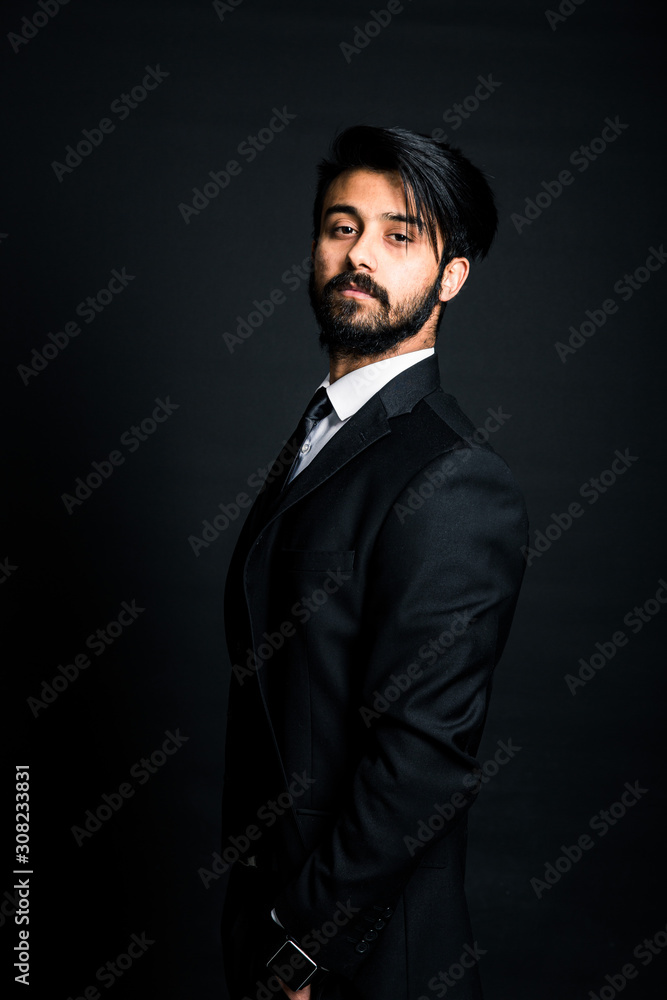 Fototapeta premium Portrait of a young handsome successful Indian in a classic black three-piece business suit on a dark background