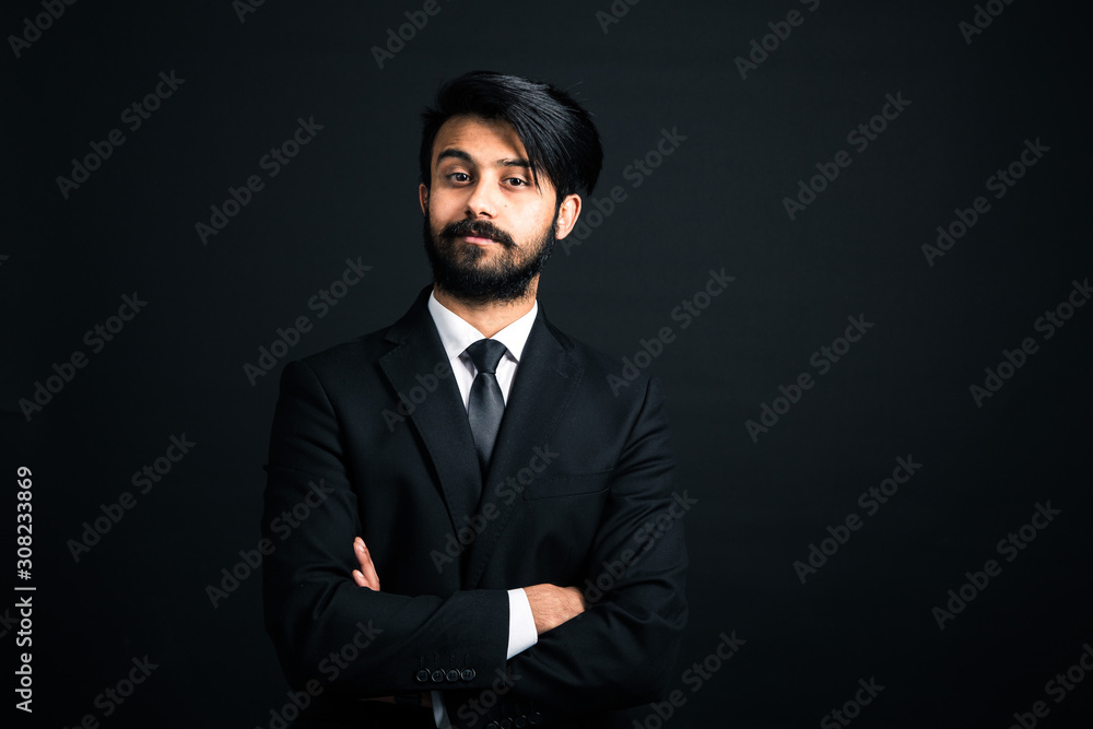 Portrait of a young handsome successful Indian in a classic black three-piece business suit on a dark background. arms crossed Portrait of a young handsome successful Indian in a classic black three-piece business suit on a dark background. arms crossed